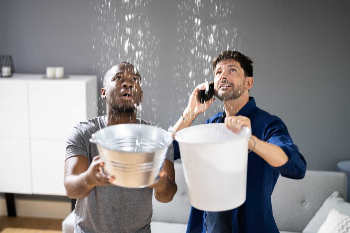 Two men holding buckets under a ceiling leak
