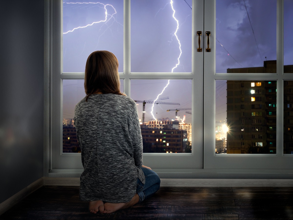 a woman looking out the window at lightning