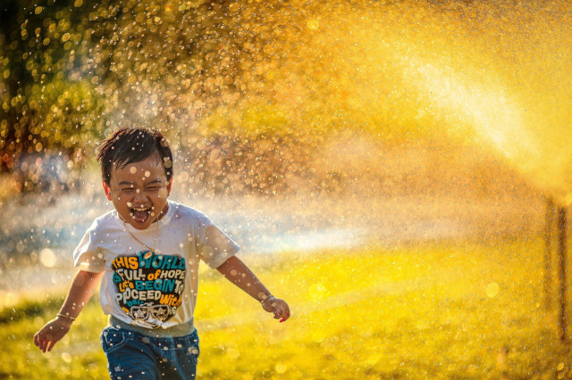 boy running in sprinkler