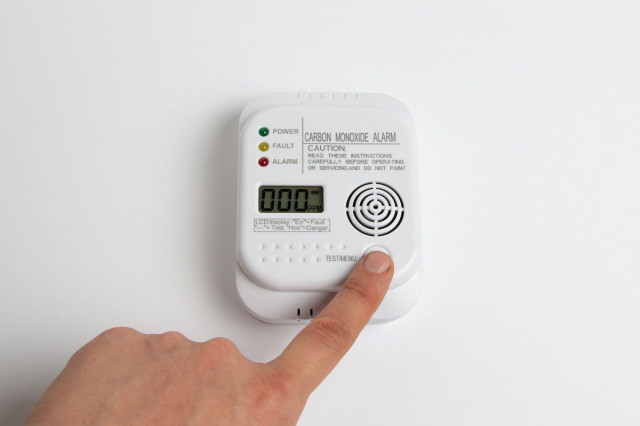 finger pressing button on carbon monoxide detector