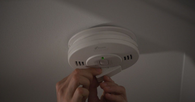 fingers pushing smoke detector button