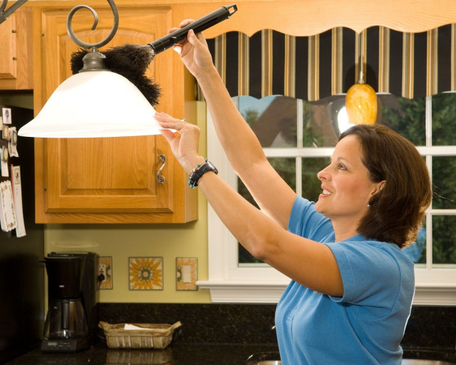 a homeowner cleaning a kitchen light fixture with a duster