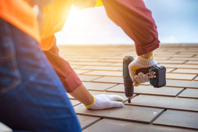 a roofer fixing a shingle with a power drill