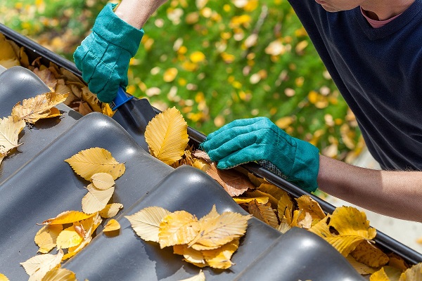 a homeowner wearing green gloves cleaning out a gutter