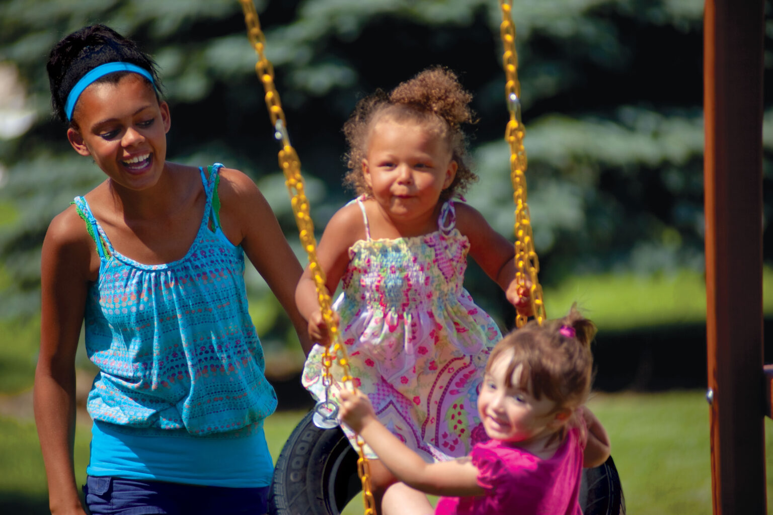2 children swinging on a tire swing being pushed by a third