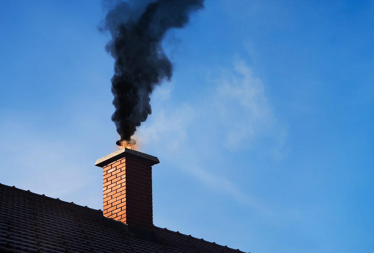 masonry chimney on a roof with black smoke coming out of it