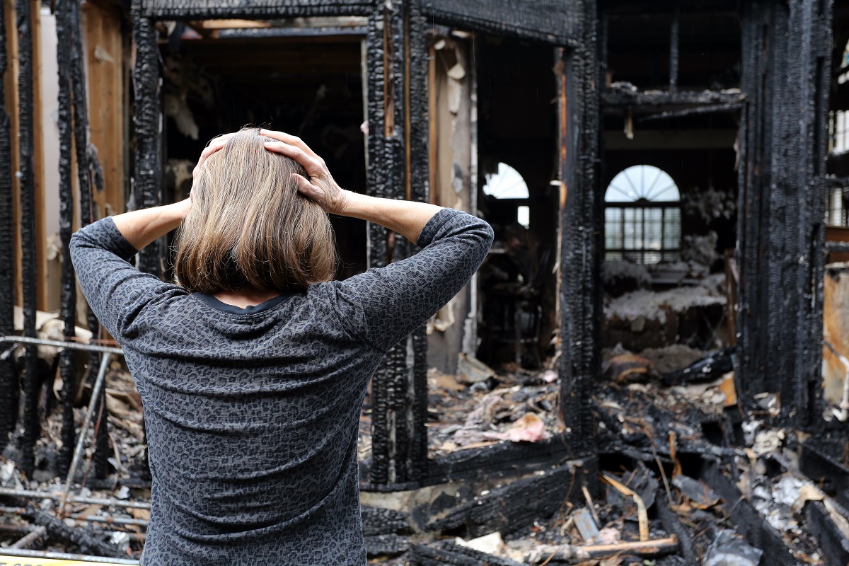 Woman clutching her head while looking at a burned down home