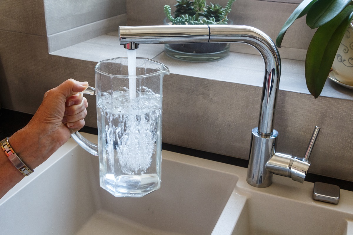 person filling up a pitcher of water from a kitchen sink
