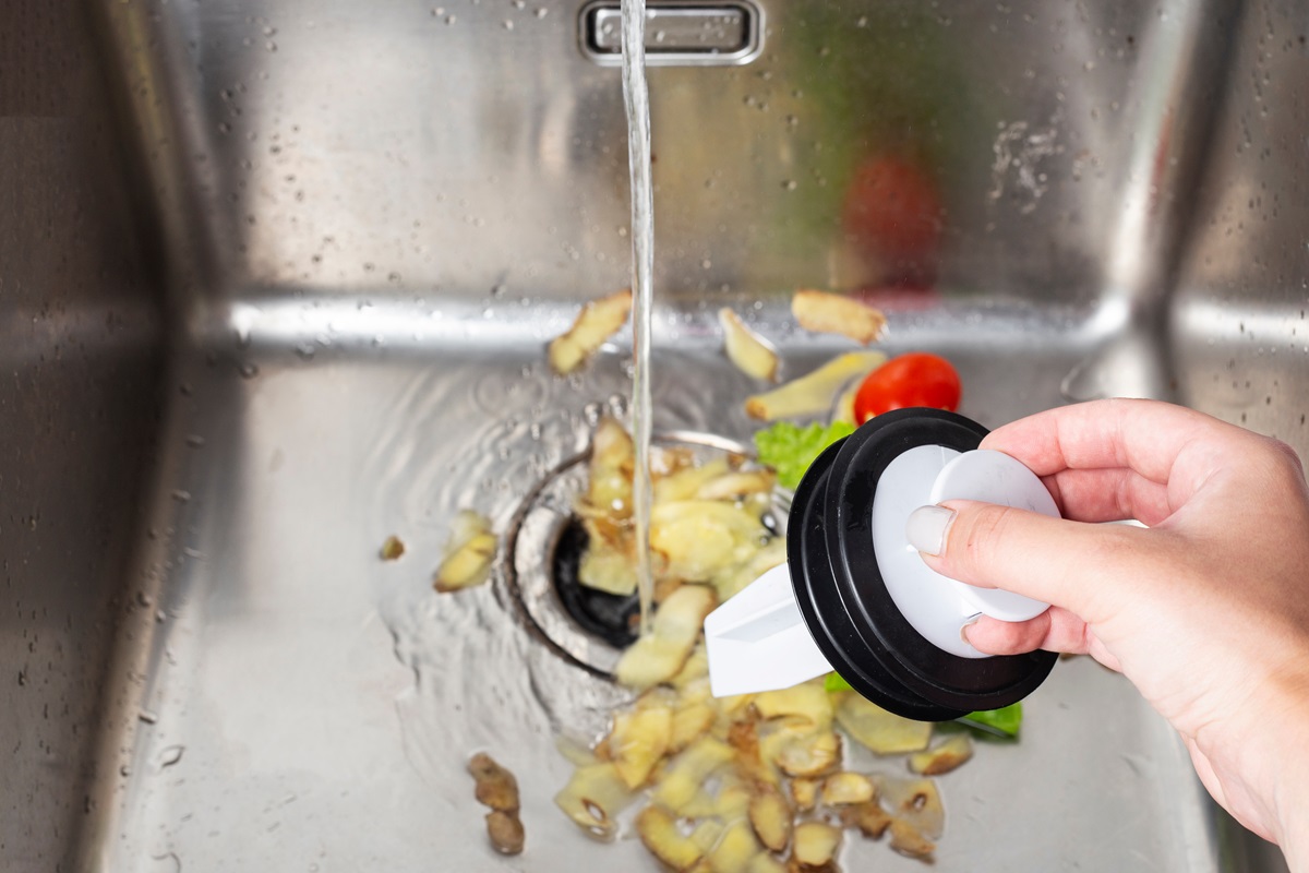a person shoving potato peels down a sink