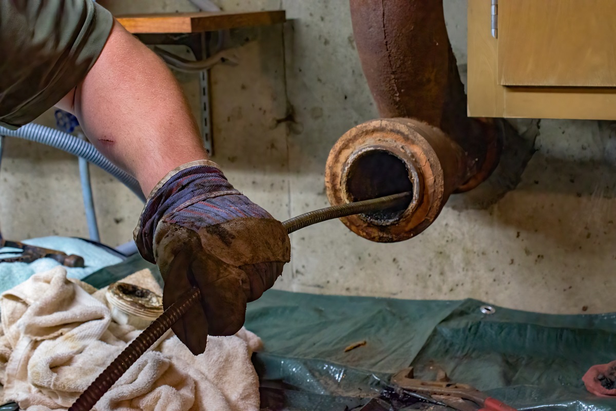 Hands of a plumber as he runs a camera scope and cleaning machine through the main pipe to unclog a pipe