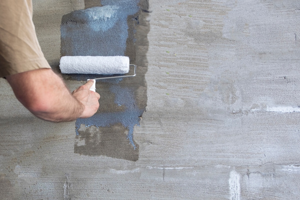 a male arm using a roller to prime a wooden wall