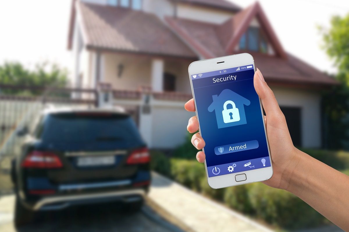 a person holding a cell phone up in front of a home and SUV. The phone has a lock on it with the words security and armed
