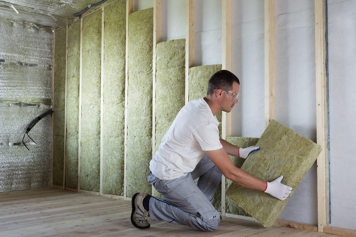 Worker in protective goggles and respirator insulating rock wool insulation in wooden frame for future house walls for cold barrier