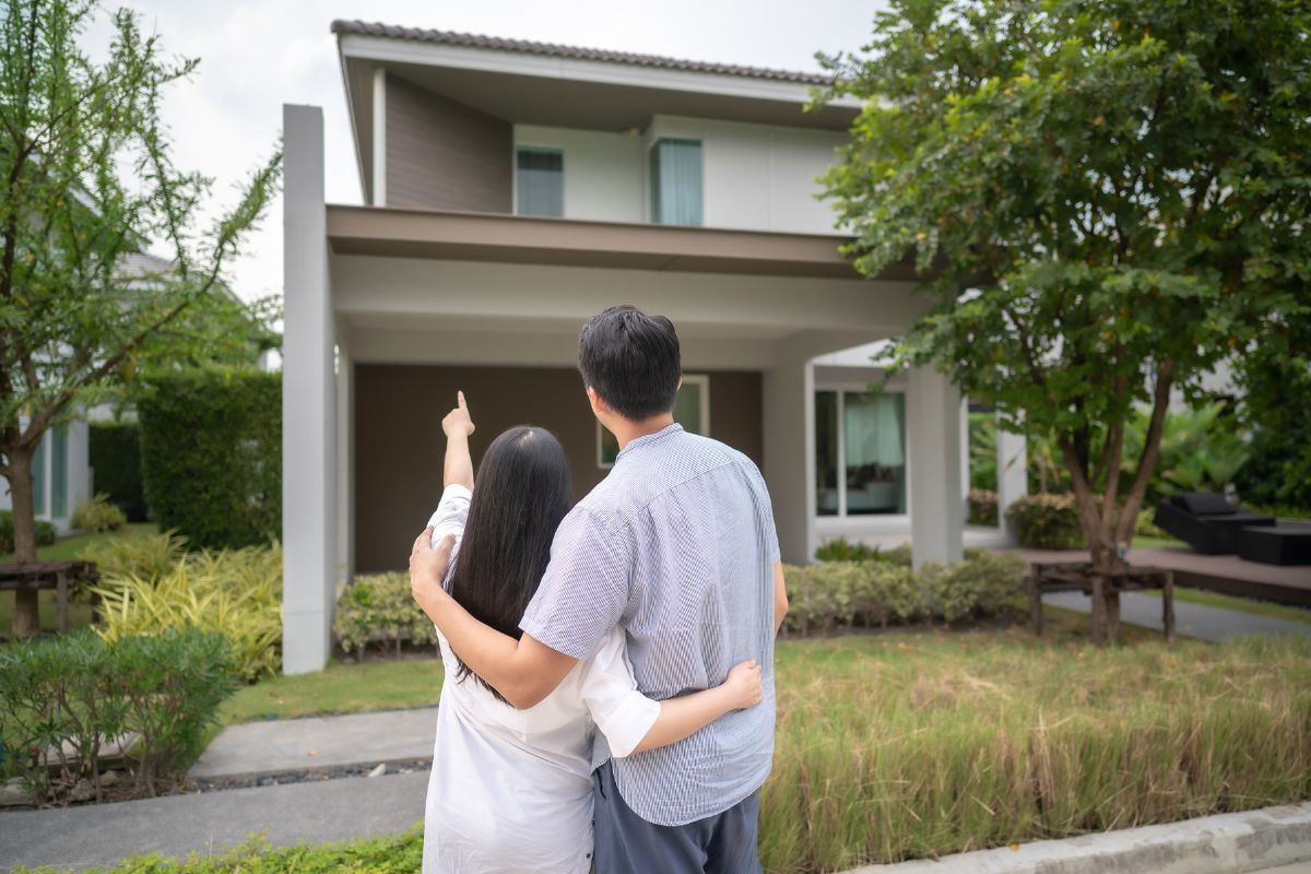 a couple standing in front of their home with their back toward us, woman pointing at elegant home
