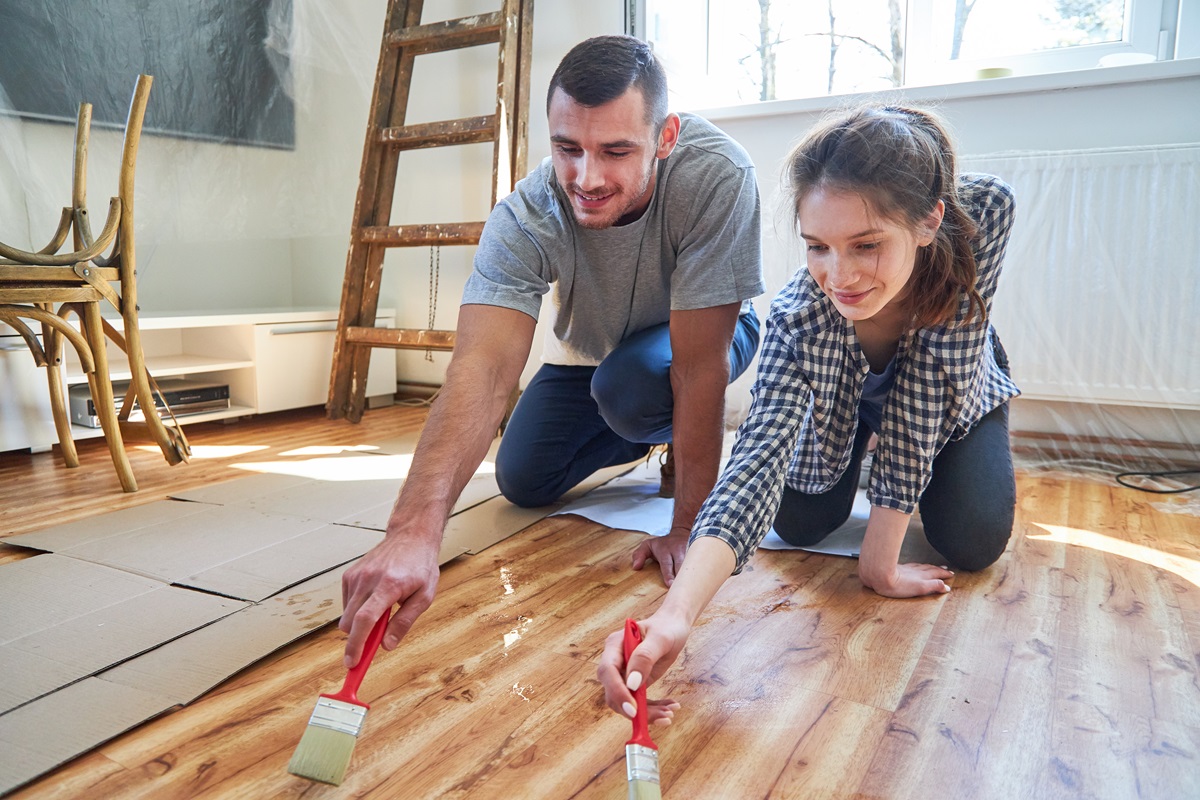 Young couple renovating in their new home together, staining hardwood floors