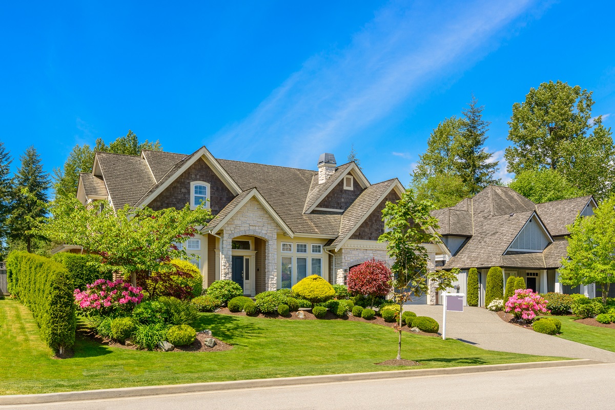 a brick and stone home with a green, well-maintained yard with a blue sky overhead