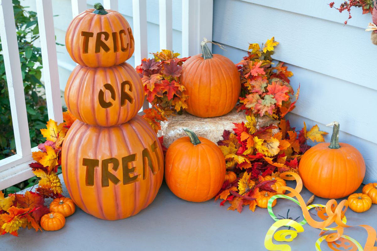 A porch with pumpkins and leaves - three stacked pumpkins read trick-or-treet