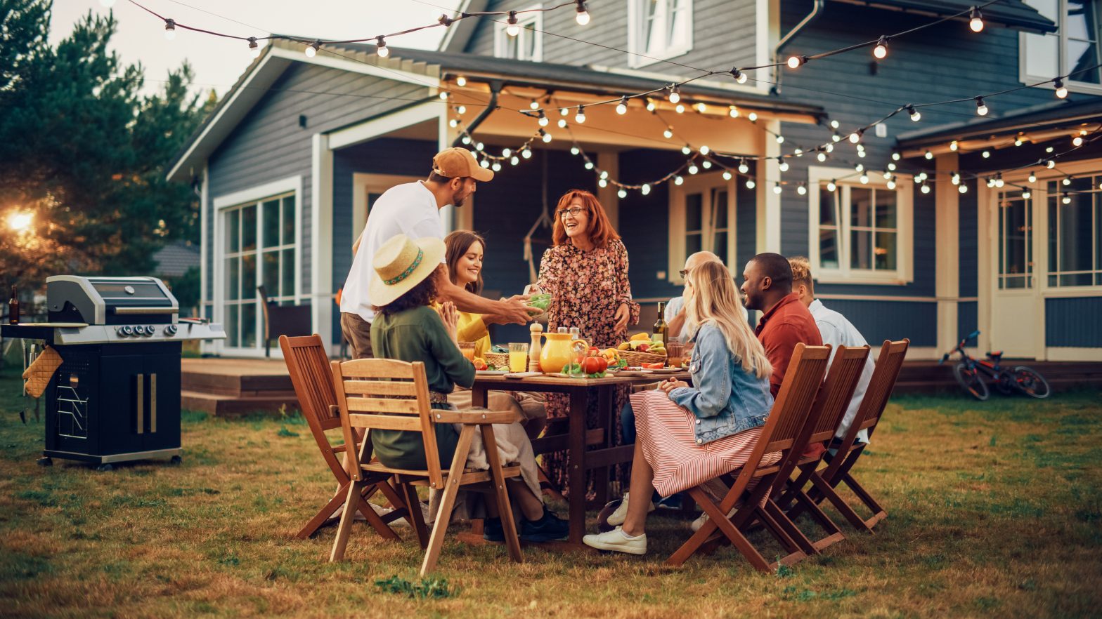 A family in their backyard around a table with a grill to the lefthand side